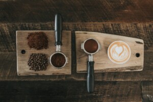 Coffee setup with coffee beans, ground coffee, and a cappuccino on a wooden surface