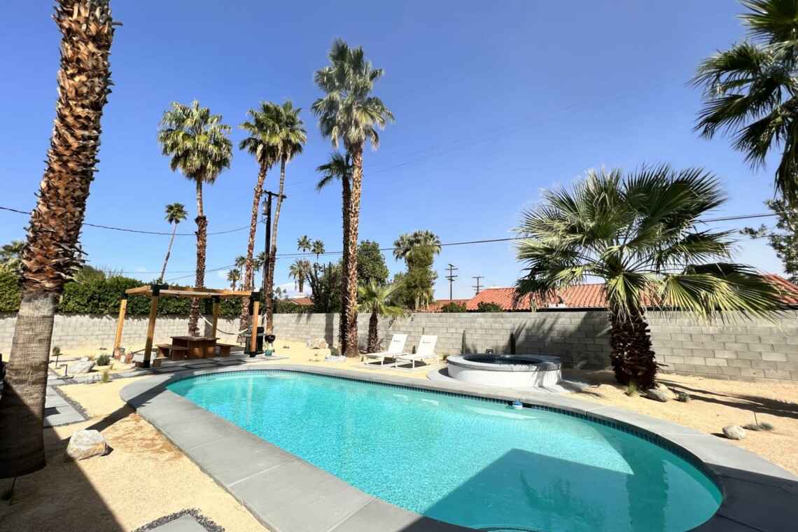 Outdoor pool area with palm trees, lounge chairs, and a pergola in a sunny setting