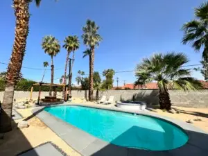 Outdoor pool area with palm trees, lounge chairs, and a pergola in a sunny setting