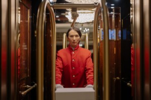 Hotel bellhop in red uniform in front of a hotel.