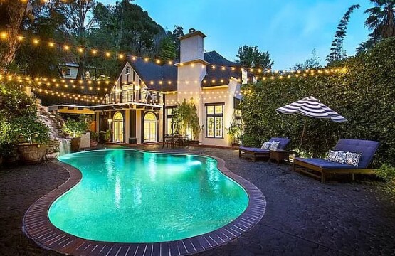 Outdoor pool area with a house in the background, surrounded by lounge chairs and greenery - by Open Air Homes.