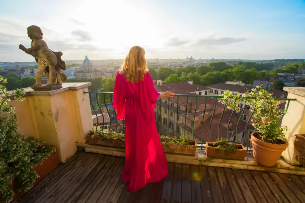 Person in red dress standing on balcony overlooking cityscape - by Open Air Homes.