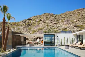 Modern house with a pool in a desert landscape, with palm trees and rocky hills – by Open Air Homes.