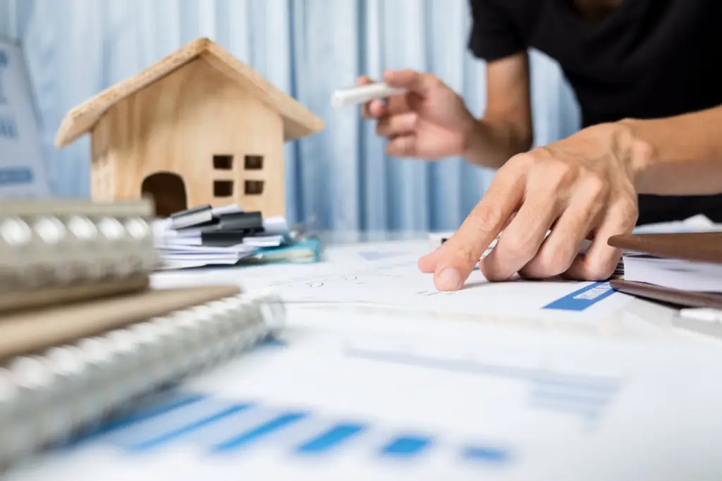 Close-up of a person pointing at documents on a table with a small house model – by Open Air Homes.