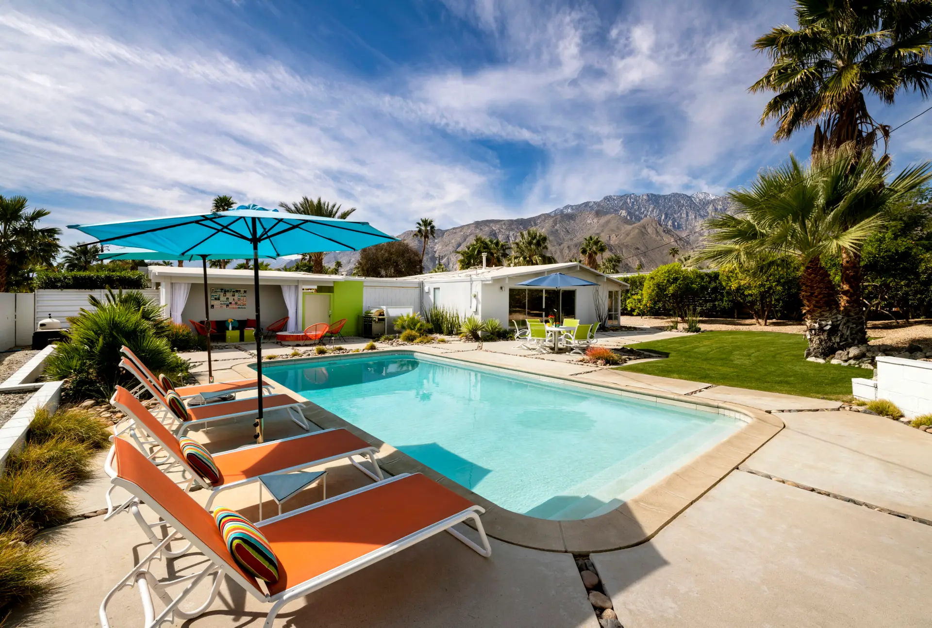 Pool area with lounge chairs, umbrellas, and modern home in a short-term rental property - by Open Air Homes.