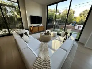 Living room with modern furniture, large TV, and sliding door leading to an outdoor area – by Open Air Homes.