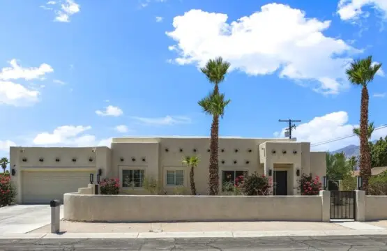 Exterior of a house with a desert landscape, palm trees, and a blue sky – by Open Air Homes.