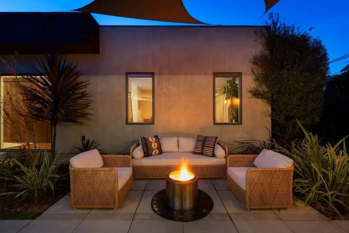 Outdoor seating area with fire pit, wicker furniture, and plants at Mar Vista Sun-Drenched Spanish Manor - by Open Air Homes.