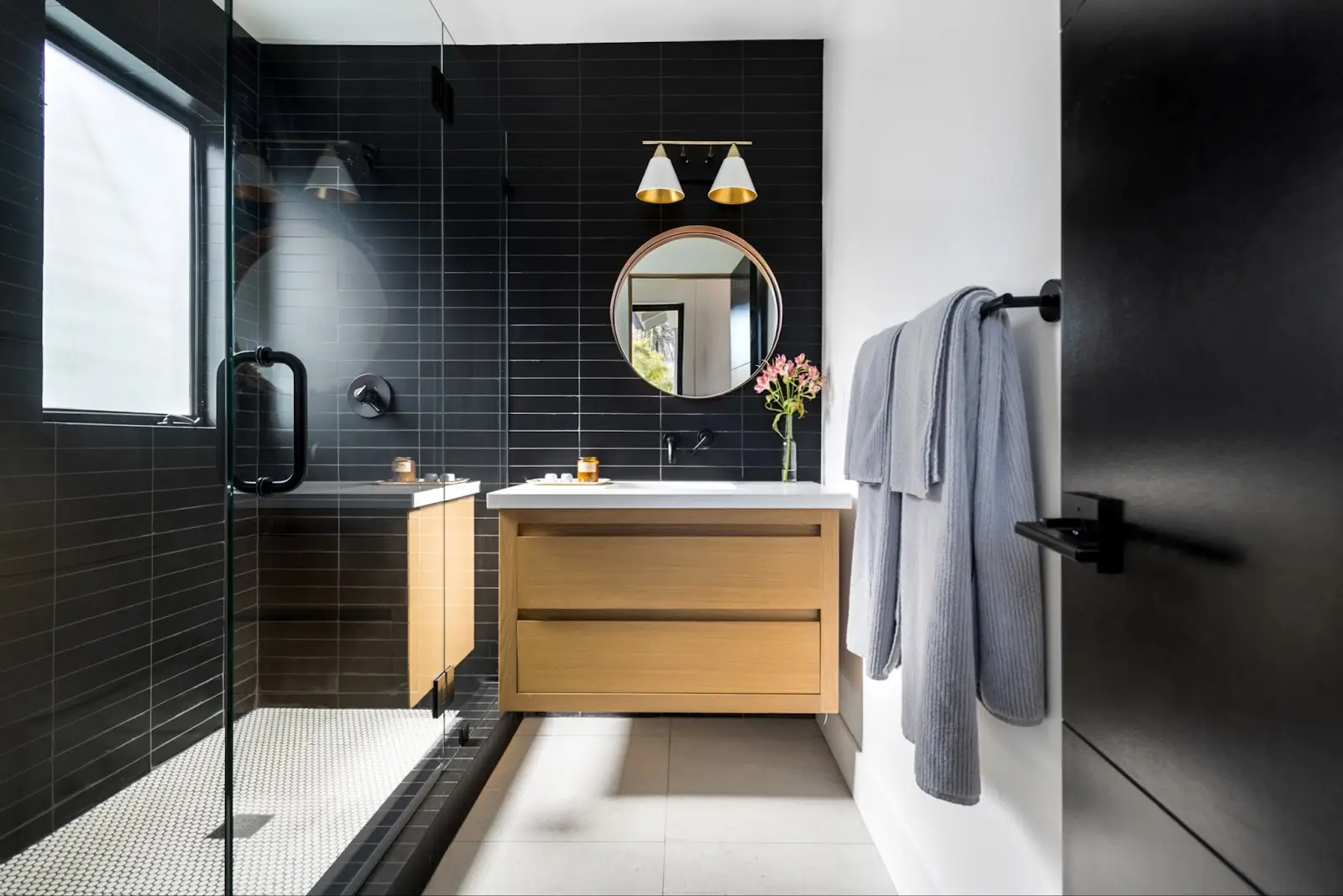 Modern bathroom with glass shower, wooden vanity, and round mirror – by Open Air Homes.