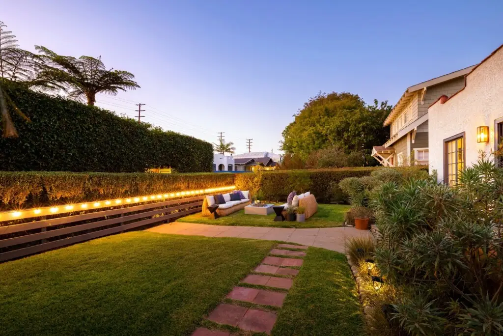 Backyard with seating area and lighting along the fence – by Open Air Homes.