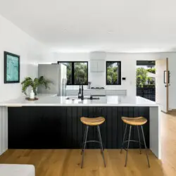 Modern kitchen with white island, bar stools, and gas cooktop at Westminster Bungalow - by Open Air Homes.Kitchen with white cabinets and black countertops at Westminster Bungalow - by Open Air Homes.