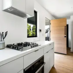 Modern kitchen with white countertop, gas cooktop, and wooden refrigerator at Westminster Bungalow - by Open Air HomWestminster Bungalow - Modern Kitchenes.