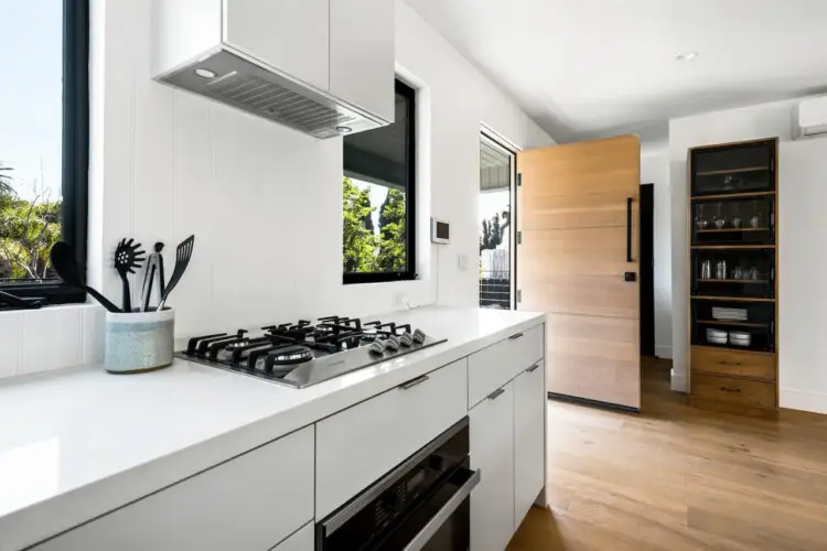 Modern kitchen with white countertop, gas cooktop, and wooden refrigerator at Westminster Bungalow - by Open Air HomWestminster Bungalow - Modern Kitchenes.