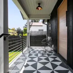 Covered outdoor patio with black and white patterned flooring, black fence, and outdoor furniture at Westminster Bungalow - by Open Air Homes.Covered outdoor patio with black and white patterned flooring, black fence, and outdoor furniture at Westminster Bungalow - by Open Air Homes.