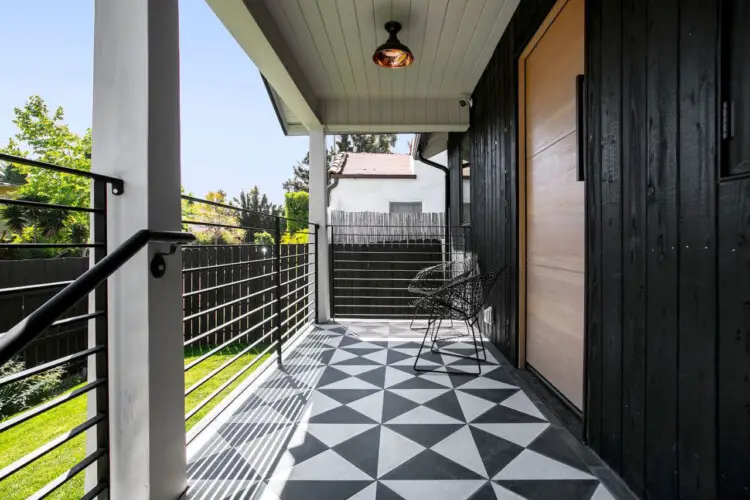 Covered outdoor patio with black and white patterned flooring, black fence, and outdoor furniture at Westminster Bungalow - by Open Air Homes.Covered outdoor patio with black and white patterned flooring, black fence, and outdoor furniture at Westminster Bungalow - by Open Air Homes.