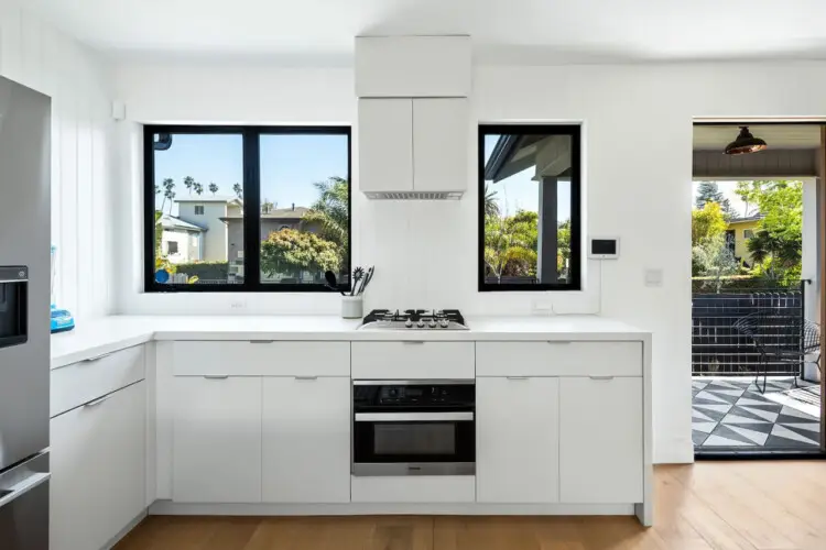 Modern kitchen with white cabinetry, gas cooktop, and large windows at Westminster Bungalow - by Open Air Homes.Kitchen with white cabinets and black countertops at Westminster Bungalow - by Open Air Homes.