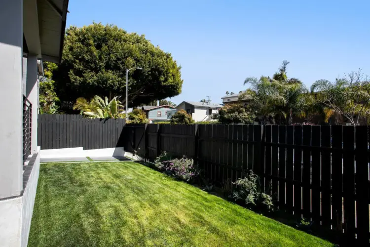 Backyard with black fence, green grass, and view of neighboring houses at Westminster Bungalow - by Open Air Homes.