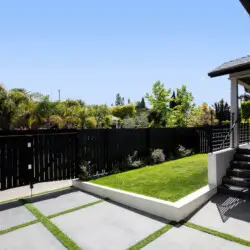 Backyard with black fence, green grass, and view of neighboring houses at Westminster Bungalow - by Open Air Homes.