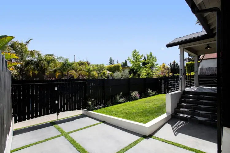 Backyard with black fence, green grass, and view of neighboring houses at Westminster Bungalow - by Open Air Homes.