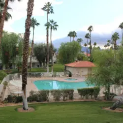 Swimming pool surrounded by a fence, palm trees, and grassy area at Desert Falls in this gated community - Family Home by Open Air Homes