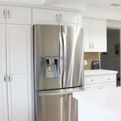 Kitchen with white cabinets and stainless steel refrigerator at Desert Falls by Open Air Homes: Family Home in Gat.