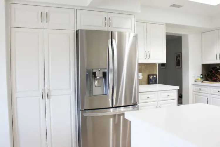 Kitchen with white cabinets and stainless steel refrigerator at Desert Falls by Open Air Homes: Family Home in Gat.