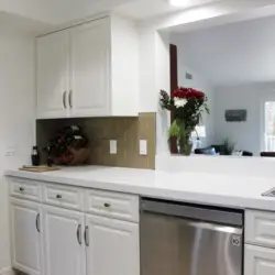 Kitchen with white cabinets, stainless steel dishwasher, and countertop with flowers at Desert Falls by Open Air Homes: Family Home in Gat.