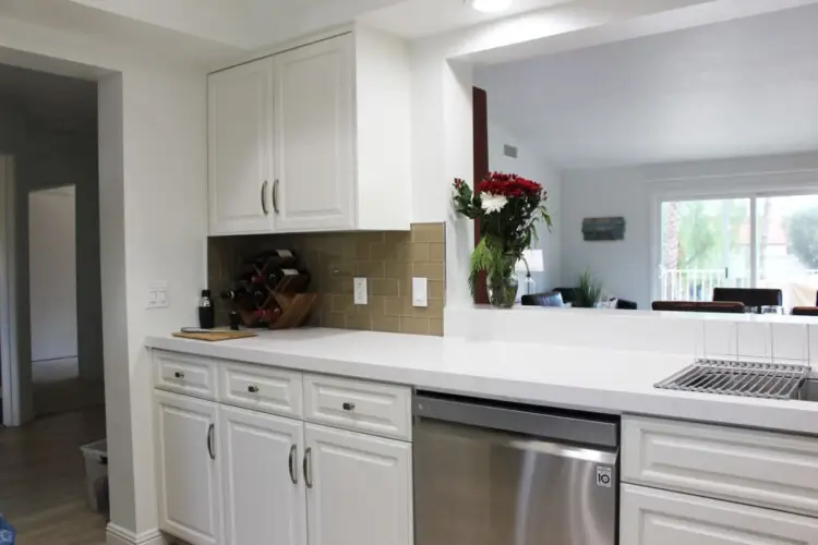 Kitchen with white cabinets, stainless steel dishwasher, and countertop with flowers at Desert Falls by Open Air Homes: Family Home in Gat.