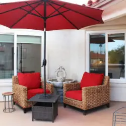 Patio with wicker chairs, small table, and red umbrella at Desert Falls in this gated community - Family Home by Open Air Homes