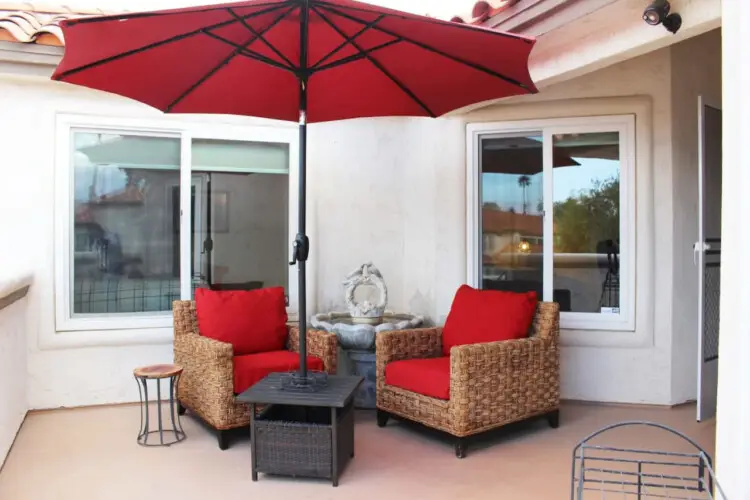 Patio with wicker chairs, small table, and red umbrella at Desert Falls in this gated community - Family Home by Open Air Homes