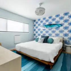 Bedroom with white bed, blue patterned wallpaper, and blue rug at Breathe Malibu - Ocean Front Condo w/ Beach Access by Open Air Homes.