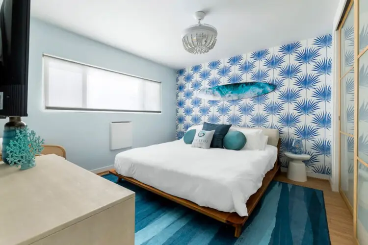 Bedroom with white bed, blue patterned wallpaper, and blue rug at Breathe Malibu - Ocean Front Condo w/ Beach Access by Open Air Homes.