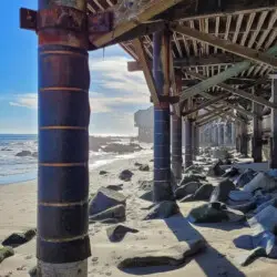 View under pier with sand, rocks, and ocean at Breathe Malibu - Ocean Front Condo w/ Beach Access by Open Air Homes.