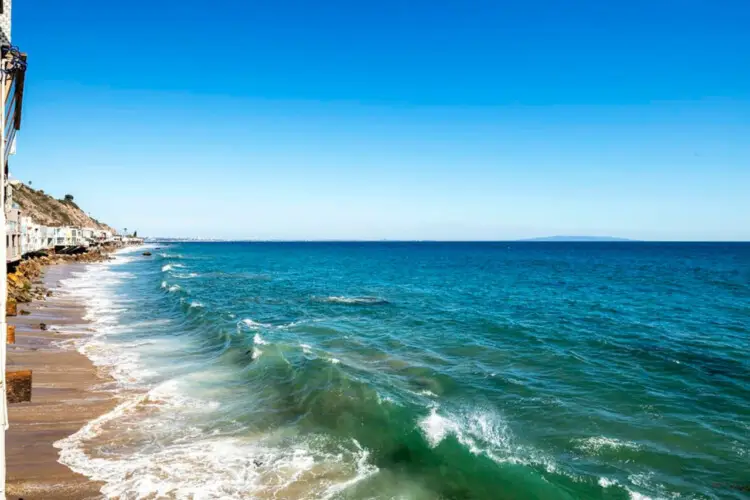 Beach and ocean view with houses along the shoreline at Breathe Malibu - Ocean Front Condo w/ Beach Access by Open Air Homes.