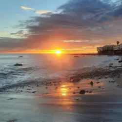 Sunset over the ocean with houses along the shoreline at Breathe Malibu - Ocean Front Condo w/ Beach Access by Open Air Homes.