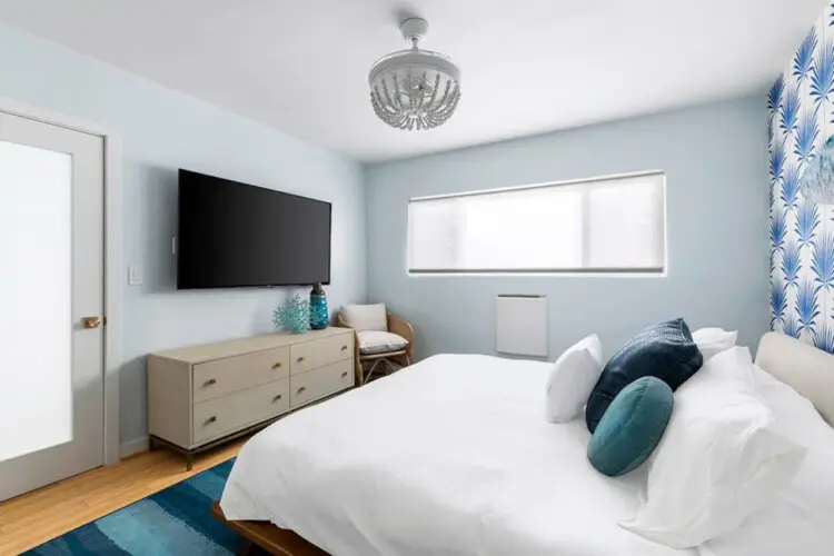 Bedroom with white bed, blue patterned wallpaper, and blue rug at Breathe Malibu - Ocean Front Condo w/ Beach Access by Open Air Homes.