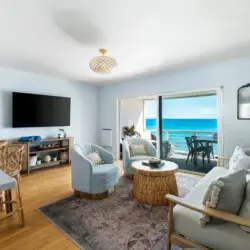 Living room with white sofa, armchairs, wicker coffee table, and ocean view at Breathe Malibu - Ocean Front Condo w/ Beach Access by Open Air Homes.