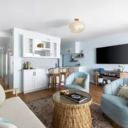 Living room with white sofa, armchairs, wicker coffee table, and ocean view at Breathe Malibu - Ocean Front Condo w/ Beach Access by Open Air Homes.