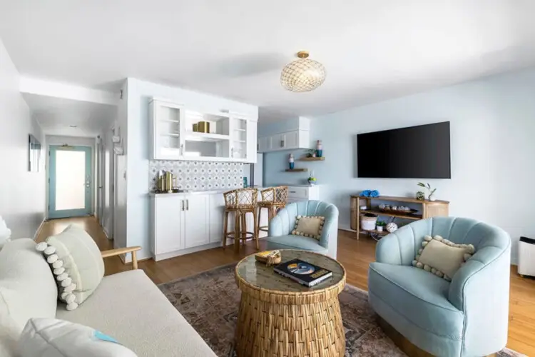 Living room with white sofa, armchairs, wicker coffee table, and ocean view at Breathe Malibu - Ocean Front Condo w/ Beach Access by Open Air Homes.