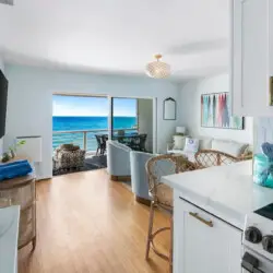 Interior view of living room and kitchen with open door leading to balcony overlooking the ocean at Breathe Malibu - Ocean Front Condo w/ Beach Access by Open Air Homes.