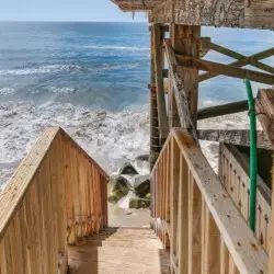 Wooden staircase leading down to the beach with ocean view at Breathe Malibu - Ocean Front Condo w/ Beach Access by Open Air Homes.