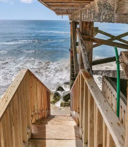 Wooden staircase leading down to the beach with ocean view at Breathe Malibu - Ocean Front Condo w/ Beach Access by Open Air Homes.