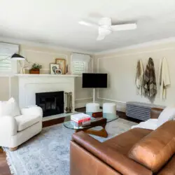 Living room with fireplace, white sofa, brown leather chair, and ceiling fan at Charming Walk Street Hideaway in Venice Beach by Open Air Homes.