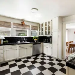 Kitchen with black and white checkeKitchen with black and white checkered flooring, white cabinets, and window at Charming Walk Street Hideaway in Venice Beach by Open Air Homes.red flooring, white cabinetry, sink, and view of dining area at Charming Walk Street Hideaway by Open Air Homes.