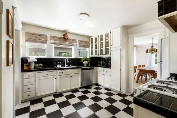 Kitchen with black and white checkeKitchen with black and white checkered flooring, white cabinets, and window at Charming Walk Street Hideaway in Venice Beach by Open Air Homes.red flooring, white cabinetry, sink, and view of dining area at Charming Walk Street Hideaway by Open Air Homes.