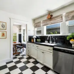 Kitchen with black and white checkeKitchen with black and white checkered flooring, white cabinets, and window at Charming Walk Street Hideaway in Venice Beach by Open Air Homes.red flooring, white cabinetry, sink, and view of dining area at Charming Walk Street Hideaway by Open Air Homes.