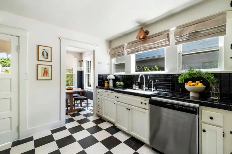 Kitchen with black and white checkeKitchen with black and white checkered flooring, white cabinets, and window at Charming Walk Street Hideaway in Venice Beach by Open Air Homes.red flooring, white cabinetry, sink, and view of dining area at Charming Walk Street Hideaway by Open Air Homes.