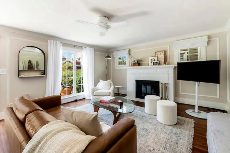 Living area with leather sofa, glass coffee table, fireplace, and wall-mounted TV at Charming Walk Street Hideaway in Venice Beach by Open Air Homes.