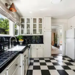 Kitchen with black and white checkered flooring, white cabinets, and black countertop at Charming Walk Street Hideaway in Venice Beach by Open Air Homes.