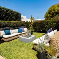 Outdoor seating area with wicker furniture and fire pit in garden at Charming Walk Street Hideaway in Venice Beach by Open Air Homes.